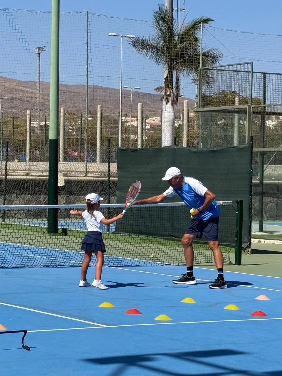 Juan guiding a young player through a volley exercise at the net